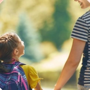 Moeder houdt lachend de hand van haar dochter vast op weg naar school